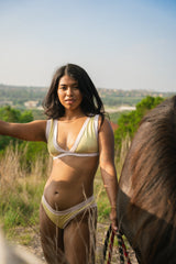 woman wearing a yellow and ivory bikini set standing next to a horse in an open field with a scenic background