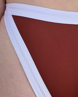 Close-up of a person wearing bikini bottoms with a rust-brown main body and a wide white waistband and side ties.