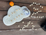 Cloud-shaped stone with Scrabble tiles spelling out words on a wooden surface.