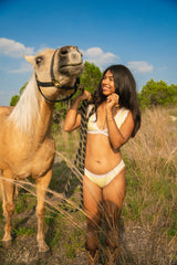Woman in a yellow bikini standing next to a horse in a natural setting