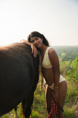 Woman in a yellow and ivory bikini standing next to a horse in a natural setting