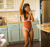 Woman wearing a brown one-piece swimsuit drinking water standing in a kitchen