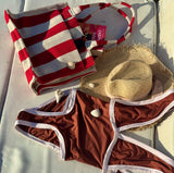 Red and white striped bag, brown swimsuit, and straw hat on a light surface