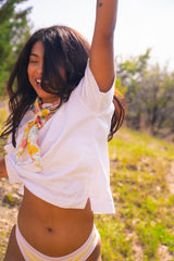 Woman in a white shirt and colorful scarf standing in a field with trees in the background
