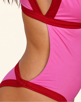 Close-up of a model wearing a bright pink one-piece swimsuit with contrasting red trim and cutout details.