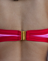 Close-up of a person's back wearing a red bikini top with a wide gold metal clasp closure and a pink lining visible along the edges.