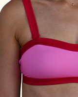 Close-up of a person wearing a two-tone bikini or sports bra top with a bright pink center panel and red straps, trim, and underband.